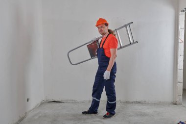 Uzun boylu, neşeli bir mühendis elinde merdiven tutuyor.