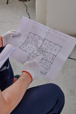 Tulum giyen bir işçi, yenileme amaçlı bir daire planına işaret ediyor.