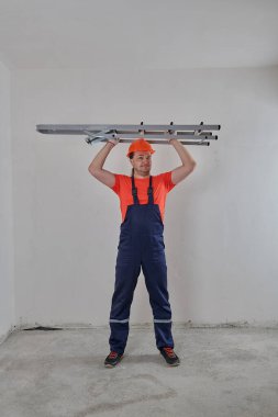 Tulumlu, miğferli bir inşaatçının elinde merdiven vardır.