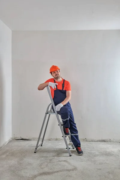 В оранжевой футболке, бригадир сидит на лестнице в шлеме — стоковое фото