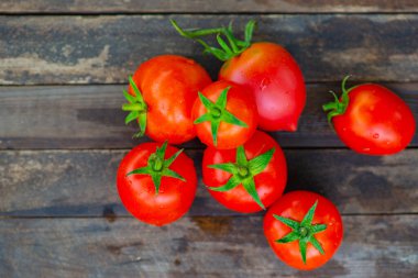 Tahta arka planda yaprakları olan parlak kırmızı domatesler.