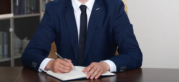 Geschäftsmann sitzt am Schreibtisch und unterschreibt einen Vertrag Stockbild