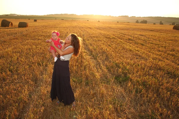 Mãe feliz segurando bebê sorrindo em um campo de trigo na luz do sol. tiro ao ar livre — Fotografia de Stock