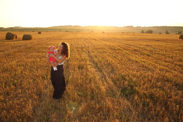 Mãe feliz segurando bebê sorrindo em um campo de trigo na luz do sol. tiro ao ar livre — Fotografia de Stock