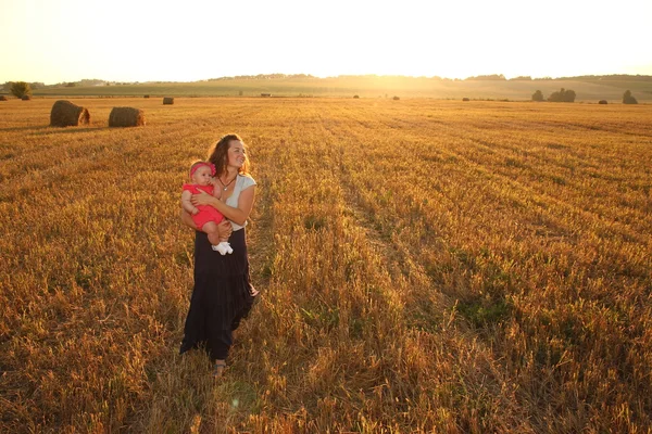 Mãe feliz segurando bebê sorrindo em um campo de trigo na luz do sol. tiro ao ar livre — Fotografia de Stock