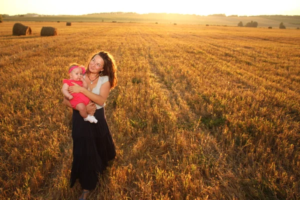 Mãe feliz segurando bebê sorrindo em um campo de trigo na luz do sol. tiro ao ar livre — Fotografia de Stock