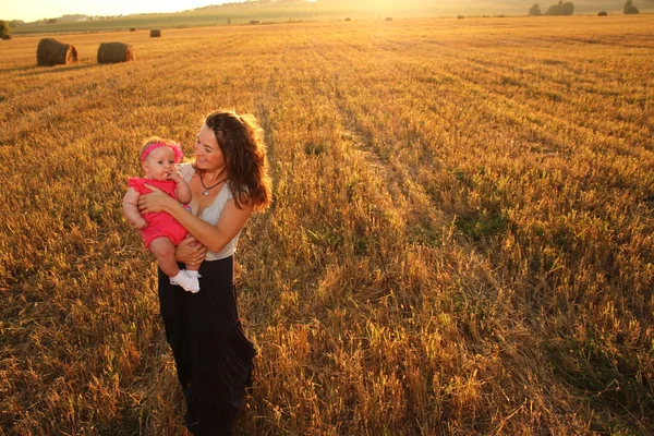 Mãe feliz segurando bebê sorrindo em um campo de trigo na luz do sol. tiro ao ar livre — Fotografia de Stock