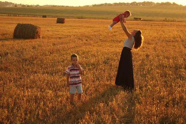 Mãe feliz segurando bebê sorrindo em um campo de trigo na luz do sol. tiro ao ar livre — Fotografia de Stock