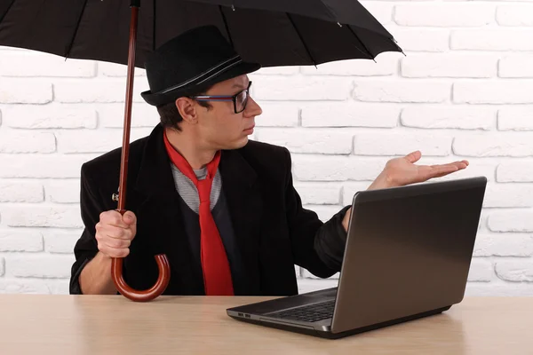 Man sitting at the table with laptop and holding umbrella — Stockfoto