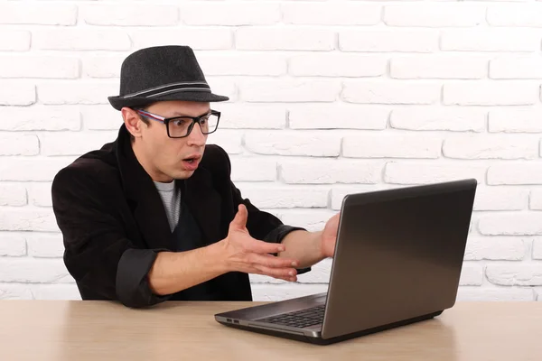 Schockierter junger Geschäftsmann, der mit seinem Laptop auf den Computerbildschirm blickt und fassungslos vor dem Büro des Unternehmens sitzt. Gesichtsausdruck, Emotion, Gefühl, Wahrnehmung, Körpersprache, Reaktion Stockbild