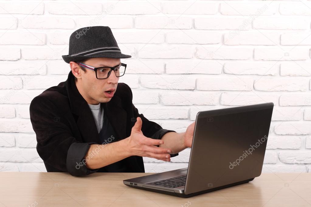 Shocked young business man using laptop looking at computer screen blown away in stupor sitting outside corporate office. Human face expression, emotion, feeling, perception, body language, reaction