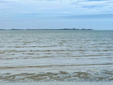 Fransa 'nın Somme Körfezi, Le Crotoy sahilinden sakin bir deniz manzarası, dalgalı dalgalar, yumuşak mavi tonlar ve bulutlu bir kıyı gökyüzü altında huzurlu bir ufuk.