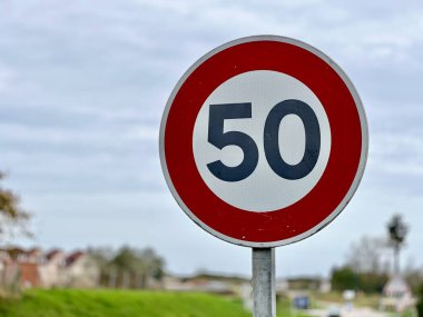 Kırmızı sınır ve beyaz arkaplan ile 50 km / saat hız limitini gösteren yuvarlak yol işaretini yakın plan, kırsal bir yol boyunca yerleştirilmiş kırsal arazi ve arka planda bulutlu gökyüzü