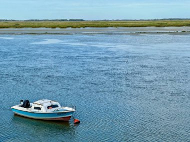 Saint-Valery-sur-Somme, Fransa - 17 Ekim 2025: Yumuşak mavi gökyüzü altında dalgalı su, tuzlu bataklık çamur ve deniz kuşları ile Somme nehrindeki bir şamandıraya demirlenmiş küçük mavi-beyaz motorlu tekne