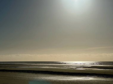 Kış plajları alçak sularda sisli güneşin altında küçük uzak yürüyüşçüler ve Fransa 'nın kuzeyindeki Opal Sahili' ndeki Mahon Kalesi 'ndeki kum düzlüklerinde parıldayan deniz yansımaları.