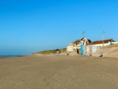 Quend, Fransa: 17 Ekim 2024: Geniş kumlu sahil ve kumsalda kumullar, deniz kenarındaki evler ve sanat deco duvar resimleriyle dolu açık mavi gökyüzü altında kuzey Fransa 'da kış öğleden sonra