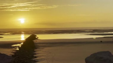 Berck, Fransa 'da Authie Körfezi' nde altın gün batımı, dalgalar ve gelgit kanallarında kayalık Groyne, yansımaları ve siluetleri ile dramatik turuncu gökyüzü