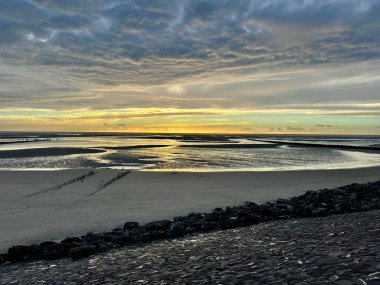 Berck, Fransa yakınlarındaki Authie Körfezi 'nin geniş manzarası gelgitte yansıtıcı kanallar ve dramatik dokulu bulutların altındaki kumsallar, ufuktaki yumuşak altın gün batımı.