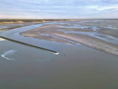 Fransa 'nın Berck yakınlarındaki Authie Körfezi' nde alçak gelgit kumsalları ve gelgit kanallarıyla birlikte yumuşak akşam gökyüzü altında dalgalanan suların yanında bir fok kolonisinin insansız hava görüntüsü.