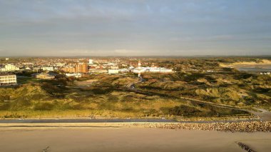 Berck-sur-Mer, Fransa 'nın insansız hava aracı panoraması, sıcak akşam ışığı altında kumlu kumlu deniz feneri, deniz kenarı ve kıyı kumullarını gösteriyor.