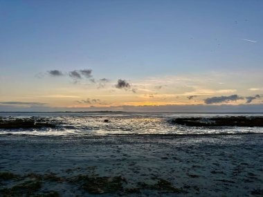 Fransa 'nın Somme Körfezi' ndeki Le Crotoy sahilinde, sakin bir sahil sahili üzerinde yansıtıcı gelgit düzlükleri, kumsallar ve dramatik bulutlar, altın ufuk.