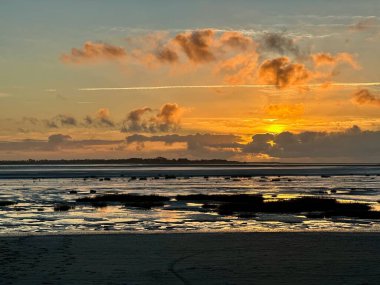Fransa 'nın Somme Körfezi' ndeki Le Crotoy sahilinde, sakin bir sahil sahili üzerinde yansıtıcı gelgit düzlükleri, kumsallar ve dramatik bulutlar, altın ufuk.