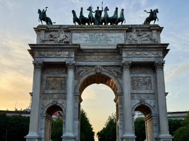 Milano, İtalya - 4 Mayıs 2025: Altın saat 'te Arco della Pace kemeri, Quadriga at heykelleri, süslemeler ve Piazza Sempione halkı ile neoklasik mermer anıt