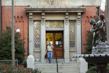 Frederick, MD, ABD 10 / 14 / 2020: Orta yaşlı bir erkek çalışan Frederick şehir merkezindeki tarihi belediye binasından ayrılıyor. Belediye binasının önünde bir heykel var..