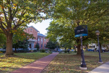 Frederick, MD, ABD 10 / 13 / 2020: Belediye binasının önündeki park. Ağaçlar, çimen tarlası, yürüyüş yolları, bir tabela direği ve arka planda tarihi belediye binası var..