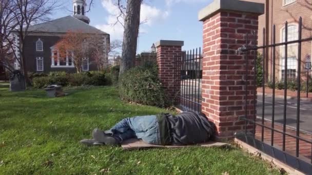 アレキサンドリア 米国11 2020 若い白人ホームレスの男性がアレキサンドリアのダウンタウンにある歴史的なキリスト教会の前の墓地の芝生の上で寝ています 男はジーンズとスウェットシャツを着ている — ストック動画