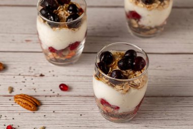 Muesli katmanları, chia tohumları, taze böğürtlen, rulo yulaf ve ahşap zemin üzerinde ev yapımı yoğurtla servis edilen ev yapımı yoğurt dolu lezzetli meyve yoğurdu parfe fincanları..