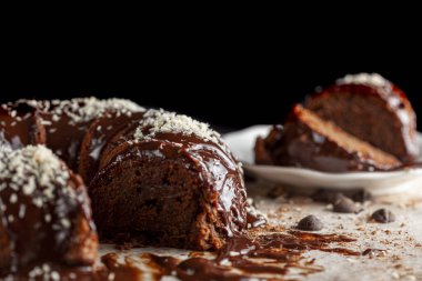 Hindistancevizi parçalı, yuvarlak çikolatalı pastanın köşeli görüntüsü. İki dilim alınıp servis için metal çatalla beyaz porselen tabağa konuldu. Yüzeyde çikolata parçaları.