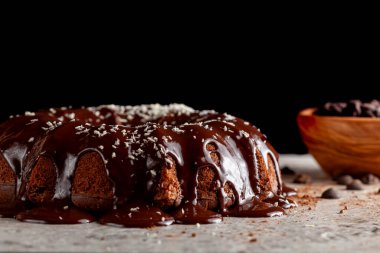 Yuvarlak çikolatalı pasta, erimiş puding kreması ve arka planda çikolata parçacıkları. Bu lezzetli pastanın süslemesi parçalanmış hindistan cevizi parçacıklarıyla tamamlanmıştı.. 