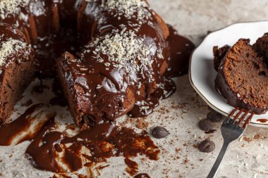 Hindistancevizi parçalı, yuvarlak çikolatalı pastanın köşeli görüntüsü. İki dilim alınıp servis için metal çatalla beyaz porselen tabağa konuldu. Yüzeyde çikolata parçaları.