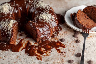 Hindistancevizi parçalı, yuvarlak çikolatalı pastanın köşeli görüntüsü. İki dilim alınıp servis için metal çatalla beyaz porselen tabağa konuldu. Yüzeyde çikolata parçaları.