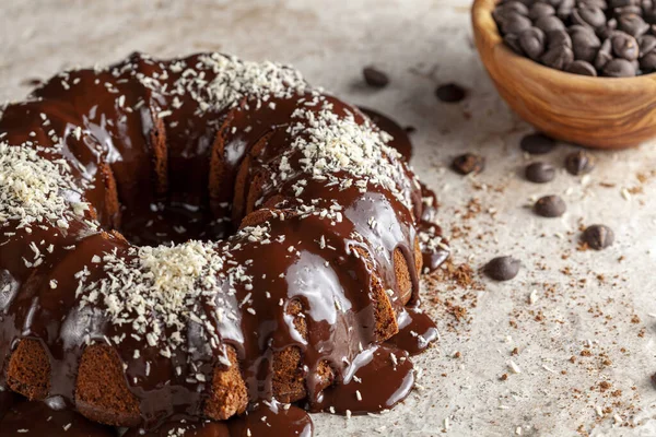 Chocolate cake with melted  pudding icing and chocolate chips in a bowl in the background. The decoration of this delicious cake was finished with sprinkles of shredded coconuts.