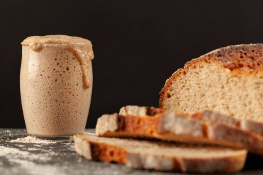 Arka planda yükselen ekşi mayalı ekmek ve taze pişmiş, ekşi hamurlu ekmek başlangıç kültürünün yan görüntüsünü kapatın. Yükselen kültür cam bardağı dolduruyor..