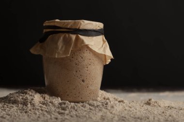 Aktif solunum nedeniyle baloncuklu cam bardak maydanoz başlangıç kültürünün yan görüntüsünü kapatın. Üstü elastik bantla sıkılaştırılmış kahverengi kağıtlarla kaplı. Arka plan karanlık..