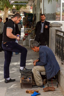 Hama, Suriye 04-02-2010: Yaşlı bir Suriyeli ayakkabı parlatıcı kalabalık bir caddenin yanındaki kaldırımda genç bir adamın ayakkabı boyama kutusuna ayakkabı boyuyor. Yaşlı adamın ellerinde boya lekeleri var..