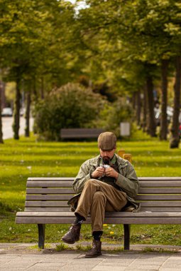Haarlem, Hollanda 06-16-2010: Klasik kıyafetler ve düz şapkalı genç bir adam park bankında tek başına oturuyor. O pipo içiyor. Keçi sakalı var.. 