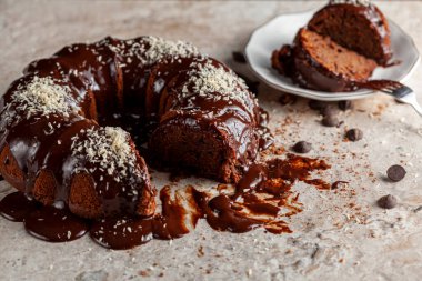 Hindistancevizi parçalı, yuvarlak çikolatalı pastanın köşeli görüntüsü. İki dilim alınıp servis için metal çatalla beyaz porselen tabağa konuldu. Yüzeyde çikolata parçaları.