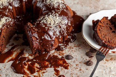 Hindistancevizi parçalı, yuvarlak çikolatalı pastanın köşeli görüntüsü. İki dilim alınıp servis için metal çatalla beyaz porselen tabağa konuldu. Yüzeyde çikolata parçaları.