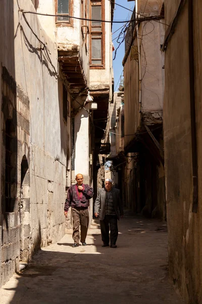 2010年3月27日 叙利亚大马士革 两名头戴宗教帽的阿拉伯老人走在大马士革古城历史建筑之间的一条狭窄小巷中 房子有窗台 — 图库照片