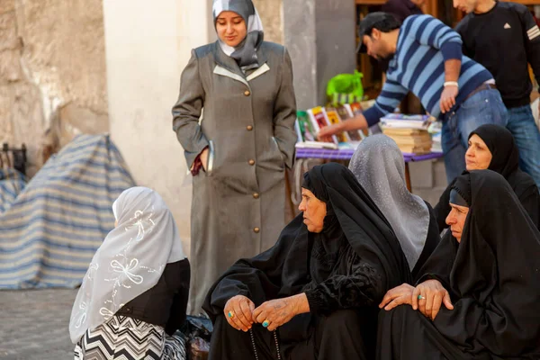 2010年3月3日至28日 叙利亚大马士革 一群身穿黑色罩袍的老年穆斯林妇女坐在集市旁的人行道上 附近还有其他有彩色装饰头巾的女人 一个人有祈祷珠子 — 图库照片