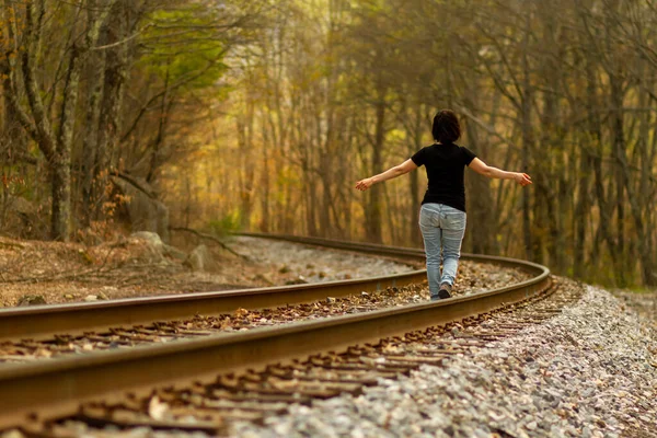 A young caucasian woman wearing jeans and t shirt is walking on the railroad tracks at a rural location with her arms wide open. A moody concept for freedom, risk taking, suicidal thoughts,