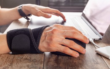 Bilgisayar faresi kullanan insanlarda bilek ekleminde kronik travma iltihaplanmaya ve ağrıya neden olan rahatsızlıklara yol açabilir. Masada çalışan bir kadın bilek desteği ve ergonomik dikey fare kullanır