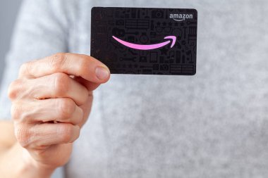Clarksburg, MD, ABD 02-25-2021: Beyaz bir kadın Amazon.com hediye kartı tutuyor (pembe logolu siyah arkaplan). Doğum günleri de dahil her olay için çok yönlü bir hediye..