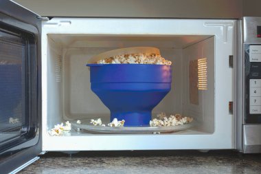 Homemade fat and salt free popcorns in a silicon BPA free collapsible popcorn popper bowl inside microwave. This bowl offers guilt free instant popcorns directly from kernels with no additives. clipart