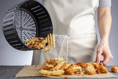 Bir kadın, tavuklu nugget ile birlikte sepetten taze patates waffle kızartmalarını tezgahın üstüne boşaltıyor. Onları çok az yağ kullanarak kızartma makinesinde kızarttı. Sağlıklı bir ev yapımı atıştırmalık..