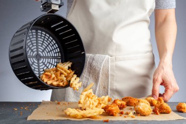 Bir kadın, tavuklu nugget ile birlikte sepetten taze patates waffle kızartmalarını tezgahın üstüne boşaltıyor. Onları çok az yağ kullanarak kızartma makinesinde kızarttı. Sağlıklı bir ev yapımı atıştırmalık..